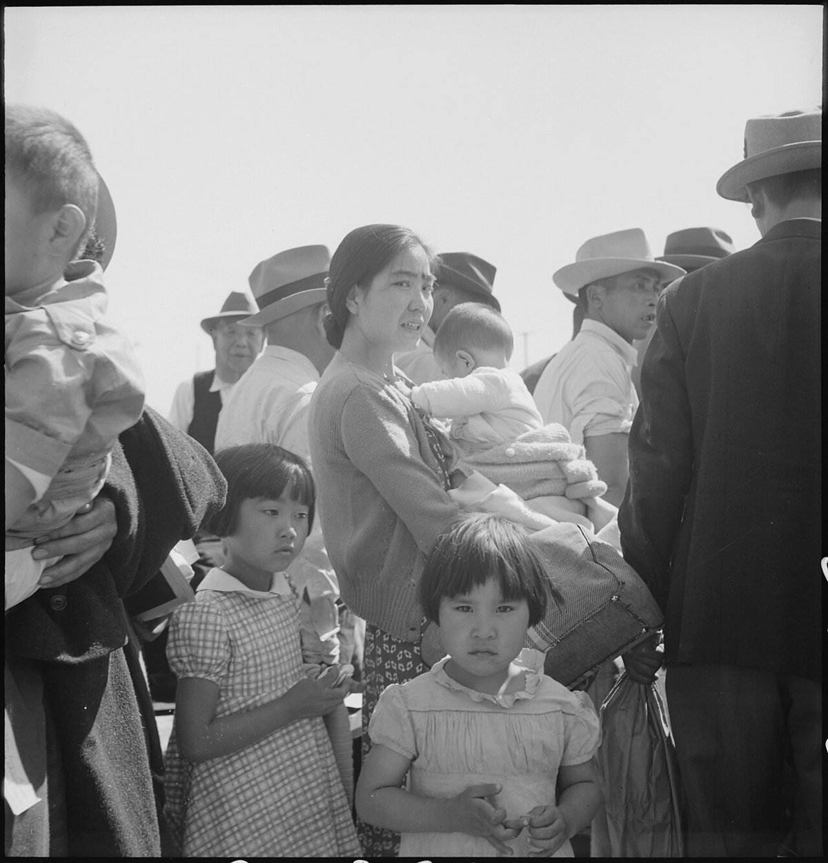 A mother holding a baby and children waiting among families arriving at the Turlock Assembly Center on May 2, 1942.