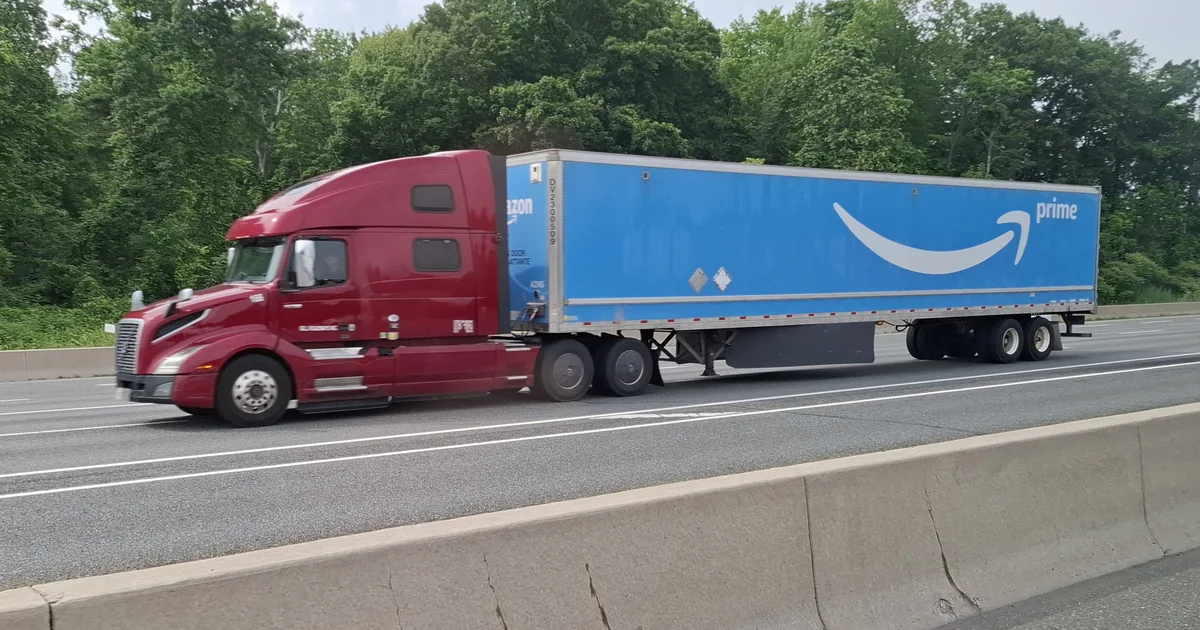 A red tractor pulling a blue Amazon Prime freight trailer on Highway 403 in Oakville, Ontario.