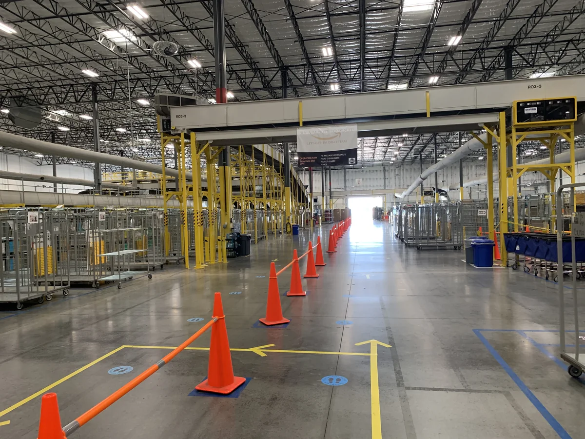 Conveyor, parcel cages and marked walkways inside an Amazon Logistics delivery station in 2020.