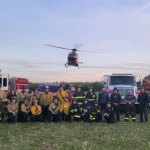 Fire crews posed in front of engines with a helicopter in the background, from the Denair Fire gallery.