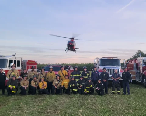 Fire crews posed in front of engines with a helicopter in the background, from the Denair Fire gallery.