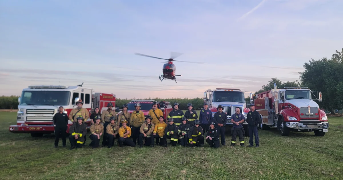 Fire crews posed in front of engines with a helicopter in the background, from the Denair Fire gallery.