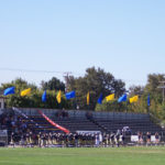 Football players and spectators beside the bleachers at Joe Debely Stadium in an older photograph.