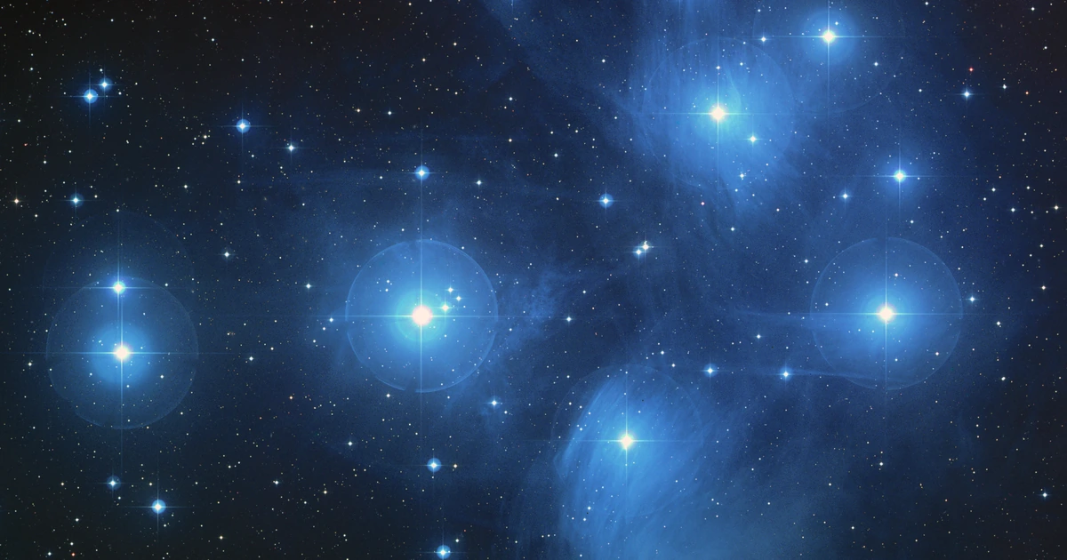 Astronomical photograph of the Pleiades star cluster with bright blue stars and surrounding reflection nebulae.